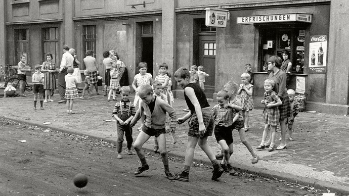 Schwarz-Weiß-Foto: Straßenszene mit spielenden Kindern vor einer Trinkhalle.