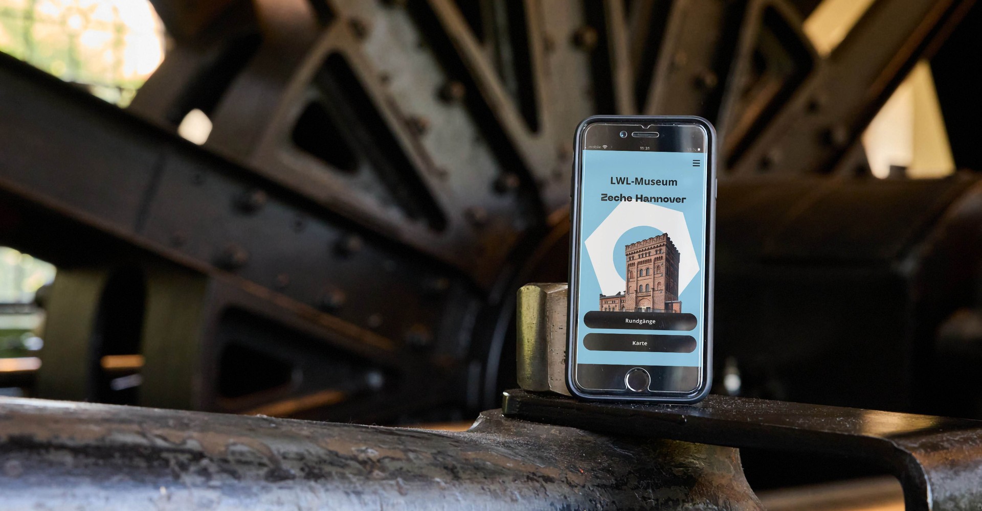 Smartphone mit der Museumsapp steht vor der Fördermaschine