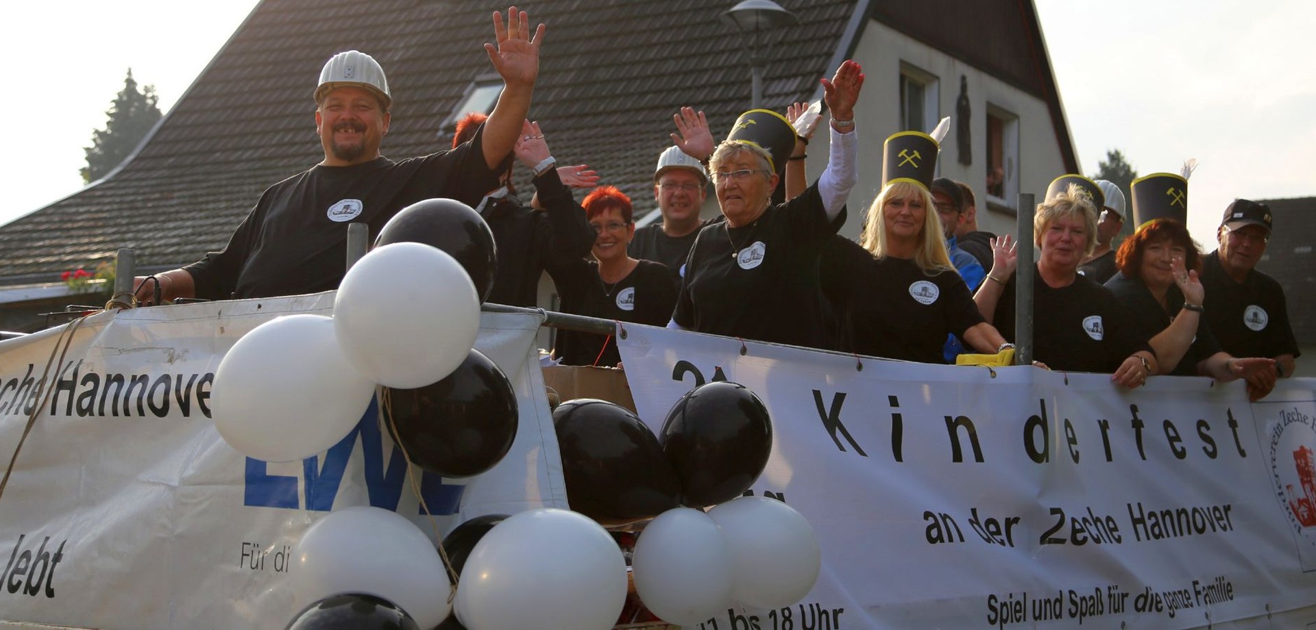 Mitglieder des Fördervereins winken auf einem offenen Wagen mit Werbung für das Kinderfest auf der Zeche Hannover.