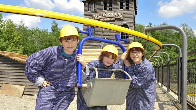 Drei Kinder in Bergmannskleidung vor einer Lore auf der Zeche Knirps