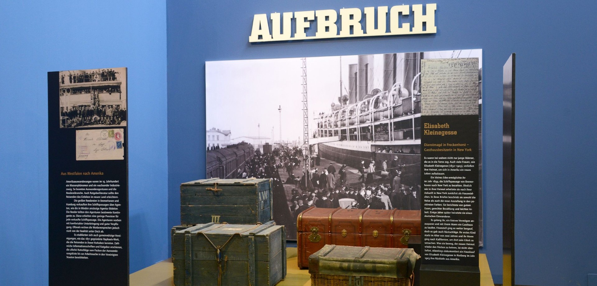 Blick in die Ausstellung "Wanderarbeit" im Ziegeleimuseum Lage. Installation mit Koffern und einem Foto eines Auswandererschiffes.