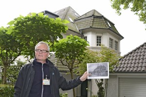 Ein Führer mit einem Foto vor einem Siedlunghaus.