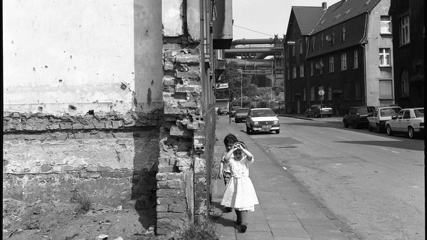 Schwarzweißfotografie einer Straße mit zwei Kindern, die über den Bürgersteig laufen