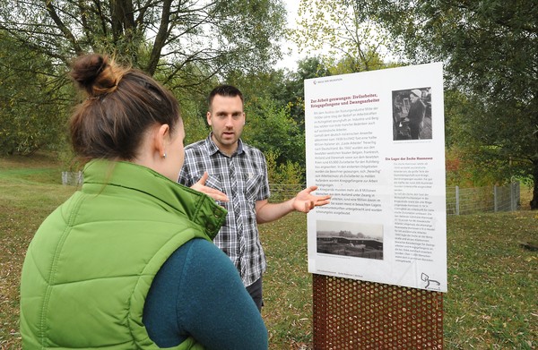 Ein Gästebegleiter mit einer Besucherin vor einer Informationstafel auf dem Rundweg zur Migration
