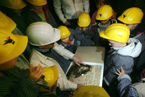 Kinder mit gelben Helmen und Bergarbeiterhemden sitzen rund um ein großes Buch