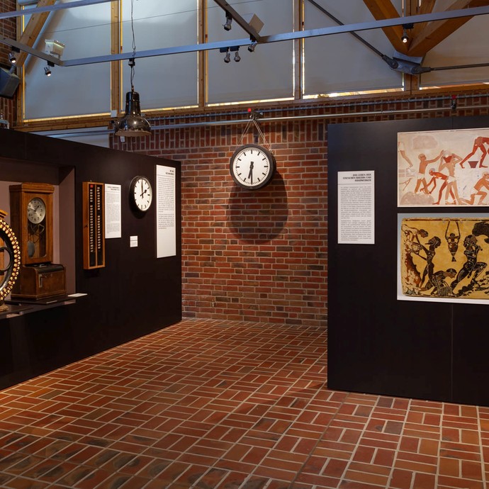 Fünf Uhren stehen und hängen in einem Ausstellungsraum. (öffnet vergrößerte Bildansicht)