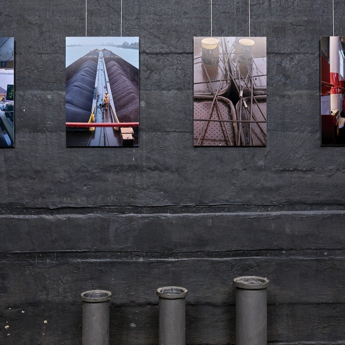 Verschiedene Fotografien hängen an einer schwarzen Wand (vergrößerte Bildansicht wird geöffnet)