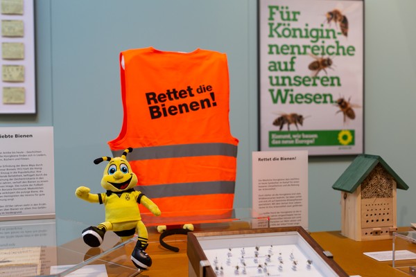 Blick in die Ausstellung: rote Warnweste mit der Aufschrift "Rettet die Bienen", BVB-Maskottchen Emma und weitere Exponate